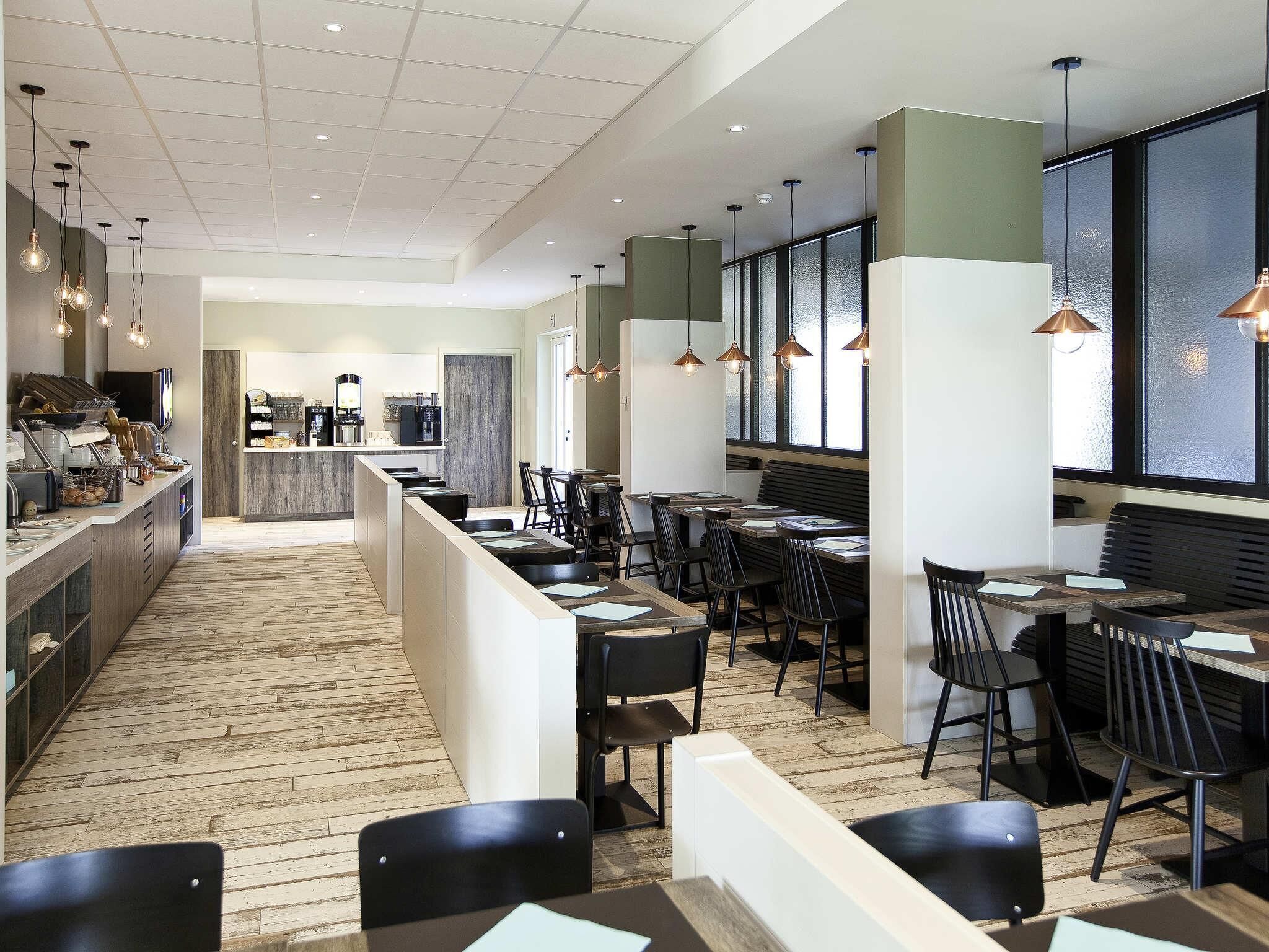 A modern restaurant with a long counter, black chairs, and pendant lighting.