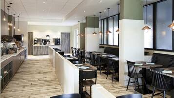 A modern restaurant with a long counter, black chairs, and pendant lighting.