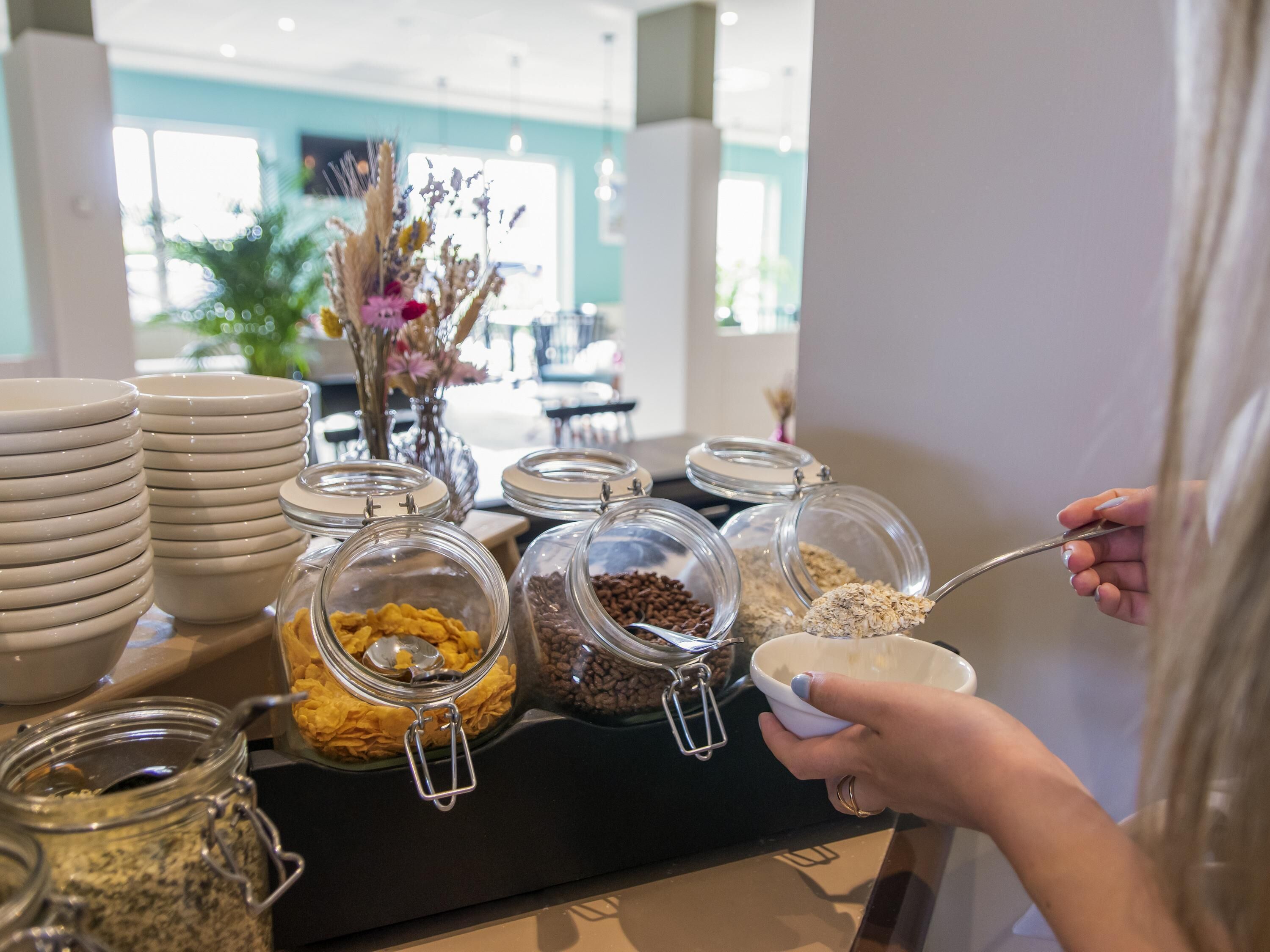 A buffet setup with various food items in glass containers, a stack of plates, and a person serving food.