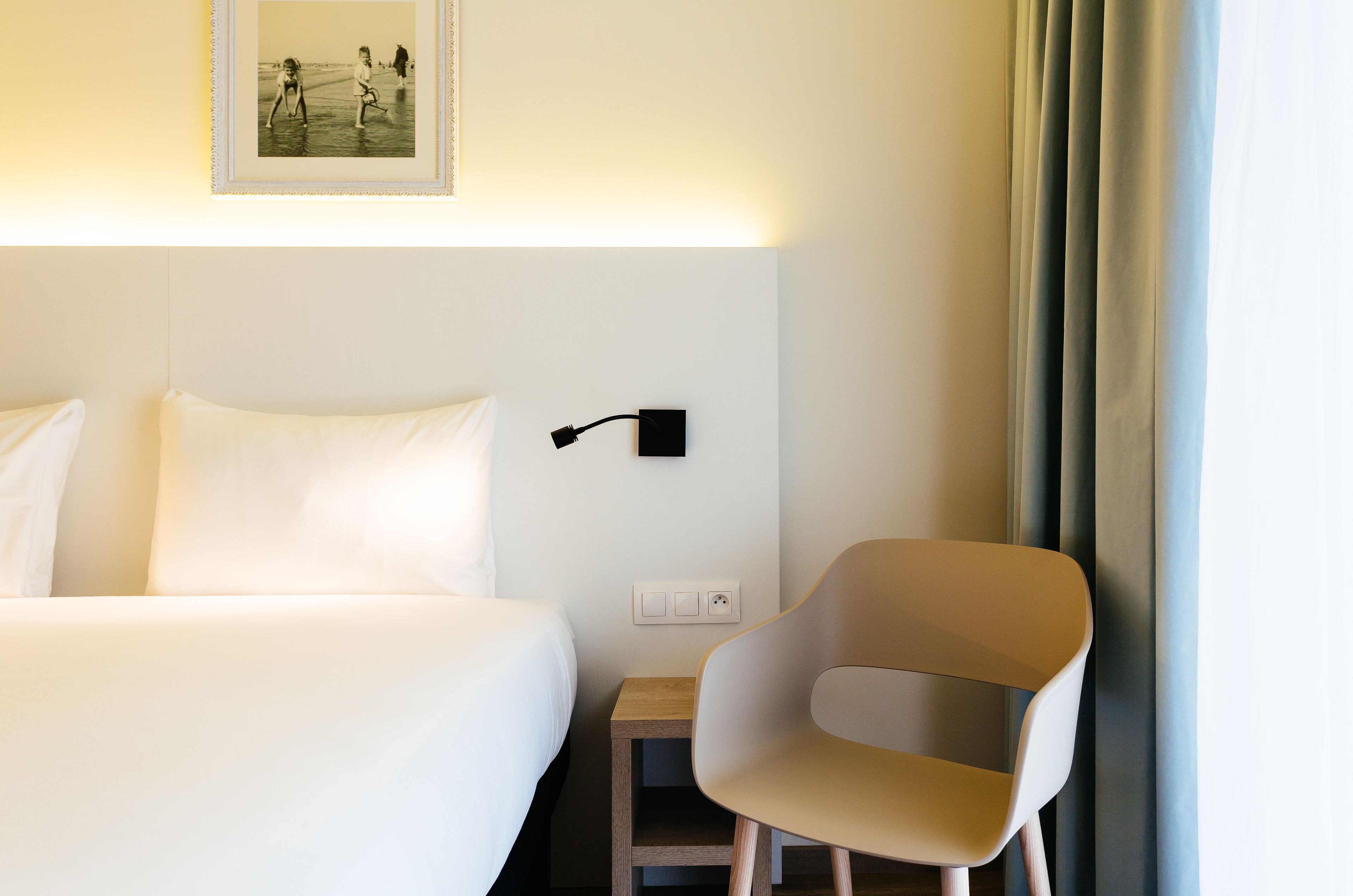 Een hotelkamer met een bed, een stoel, een wandlamp en een ingelijst kunstwerk.