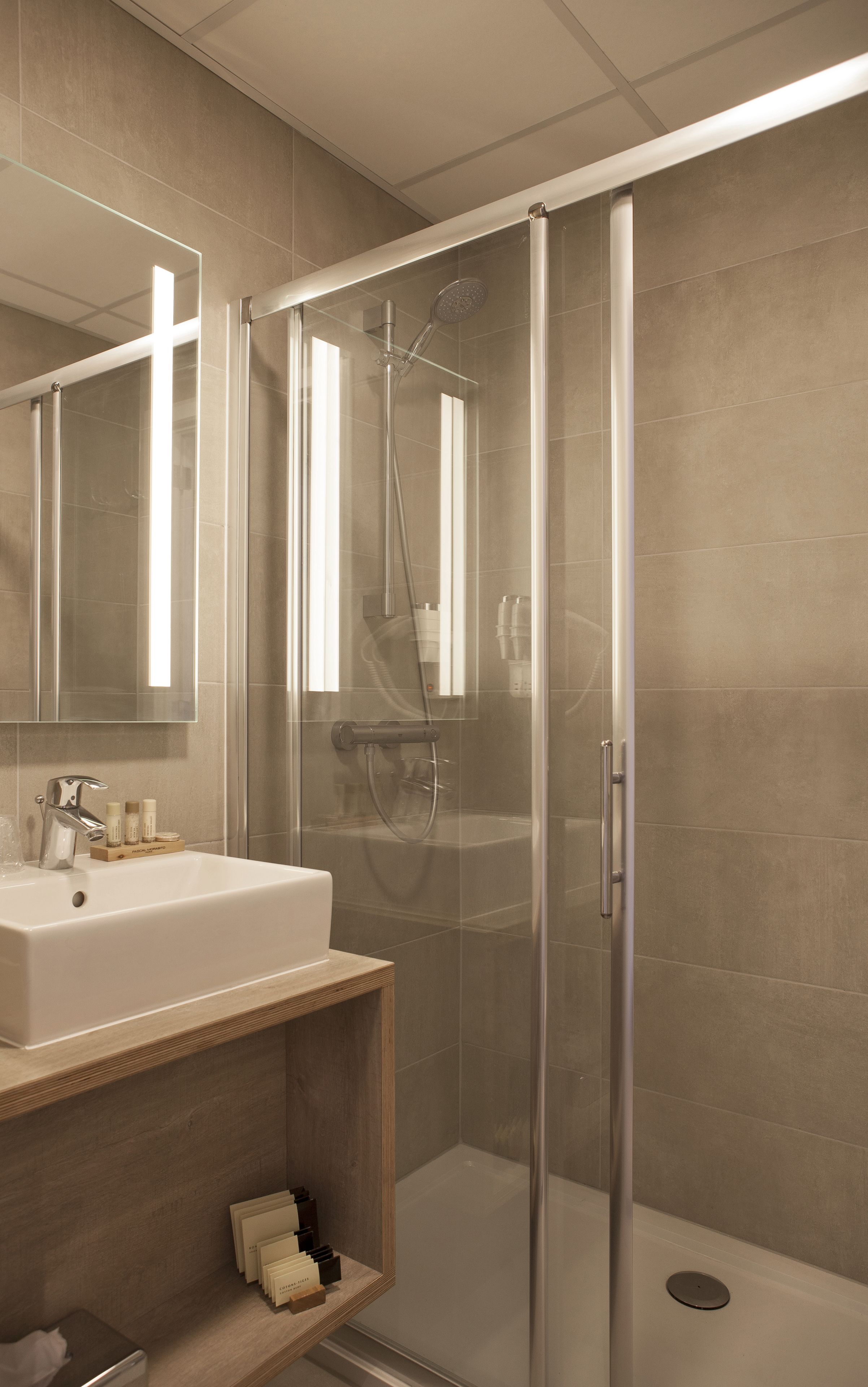 Un baño moderno con cabina de ducha de vidrio, un lavabo con artículos de aseo y un espejo.