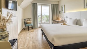A hotel room with a bed, a desk, a chair, a TV mounted on the wall, and a view of the outside balcony.