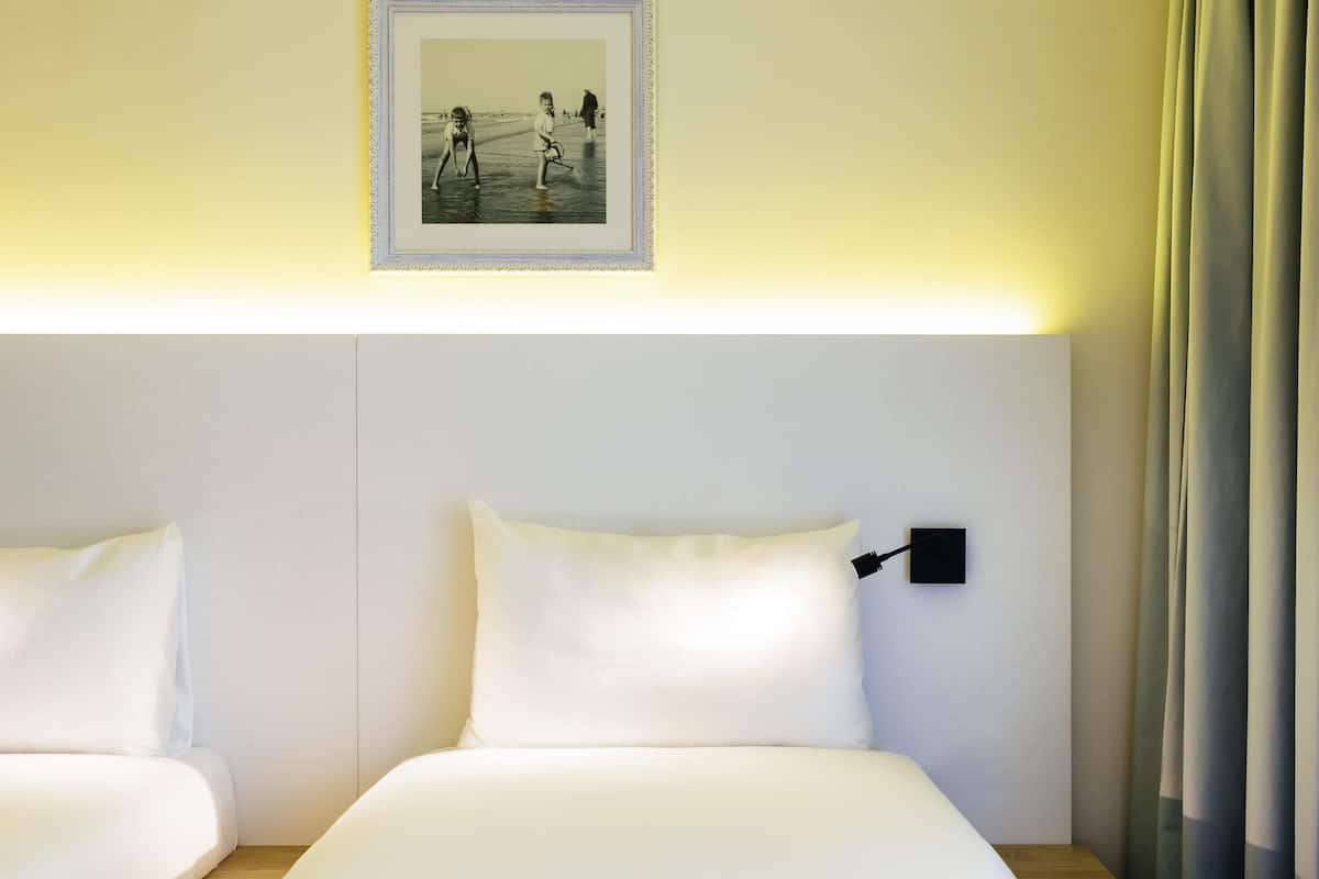 Ein Hotelzimmer mit zwei Betten, einem Nachttisch, einer Wandlampe und einem gerahmten Bild über den Betten.