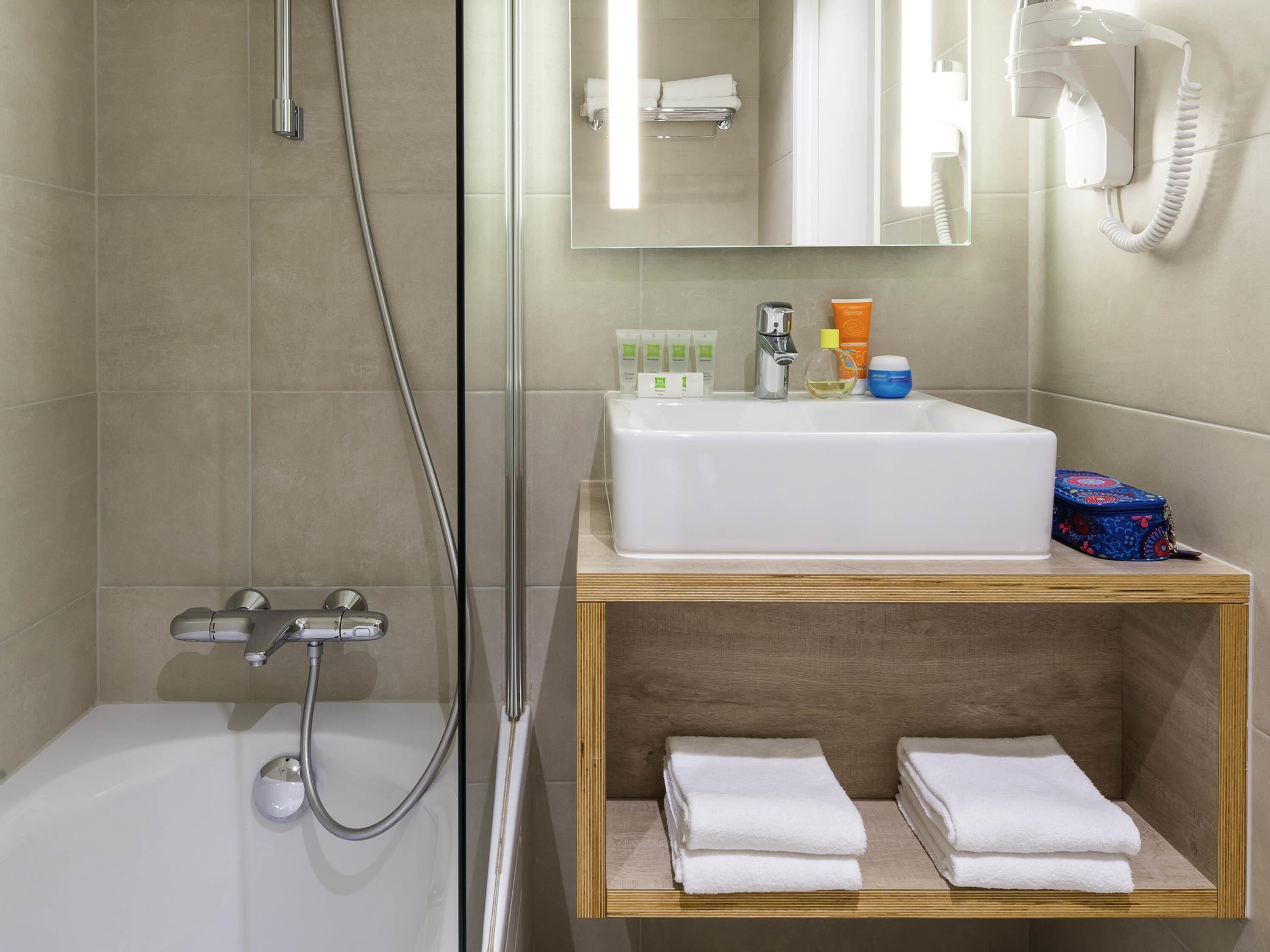 Une salle de bain équipée d’une baignoire, d’une douche, d’un lavabo avec des articles de toilette et d’un miroir.