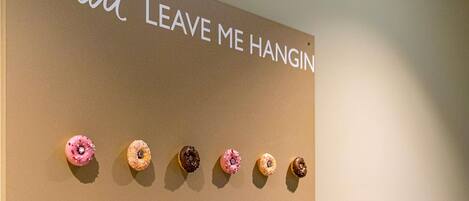 A wall with a sign that reads "donut LEAVE ME HANGIN" and a row of donuts displayed below.