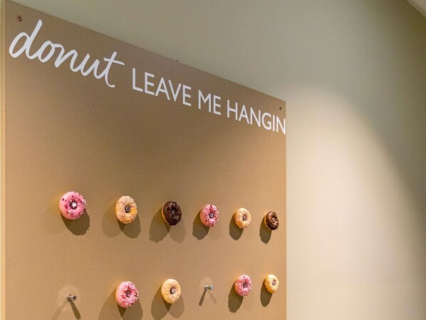 Una pared con un letrero que dice "donut LEAVE ME HANGIN" y una fila de rosquillas debajo.