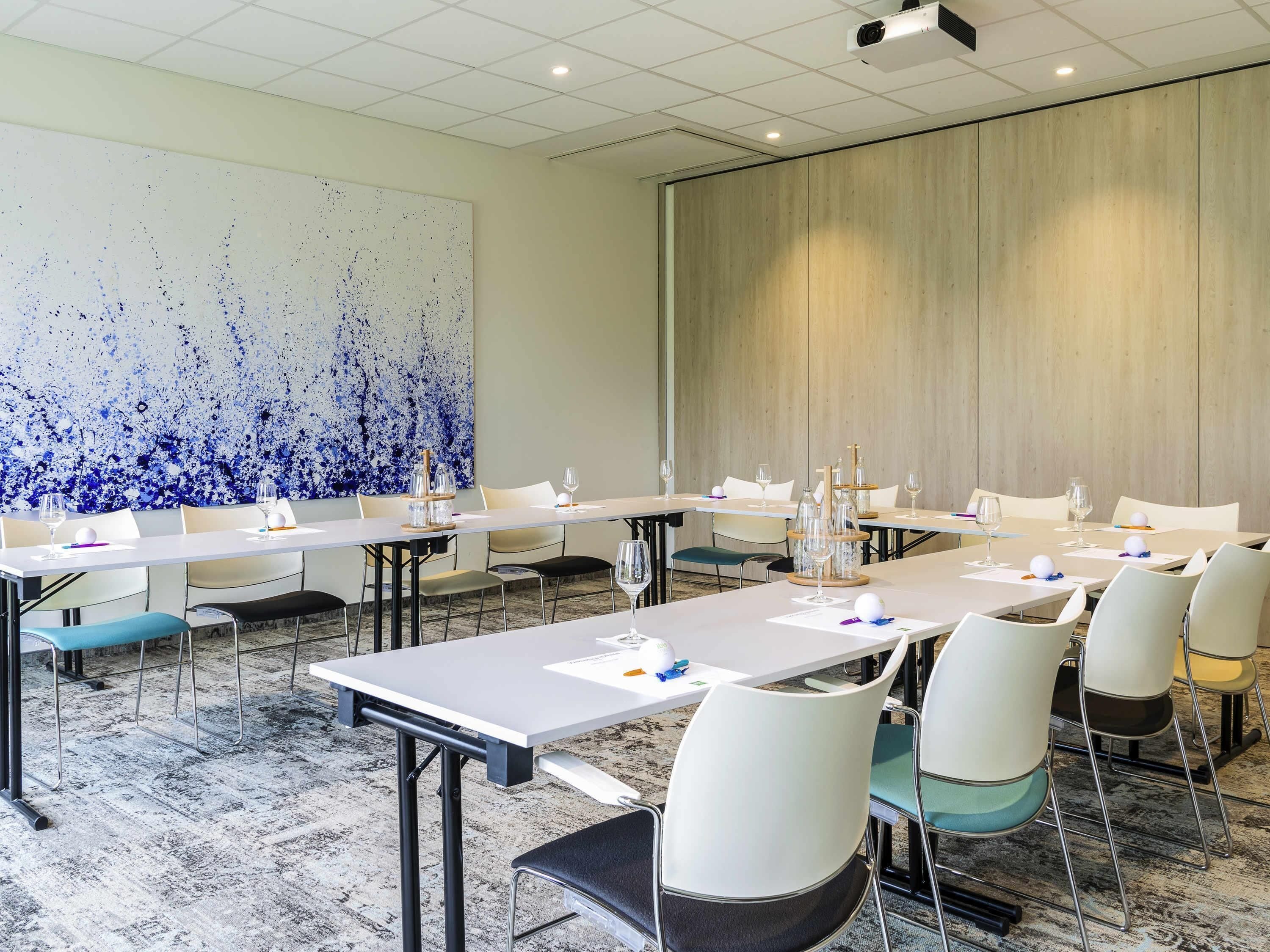 A conference room with long tables, chairs, and a large abstract painting on the wall.