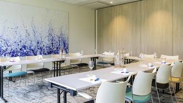 Un salón de conferencias con largas mesas, sillas y un cuadro abstracto grande en la pared.