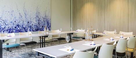 A conference room with long tables, chairs, and a large abstract painting on the wall.