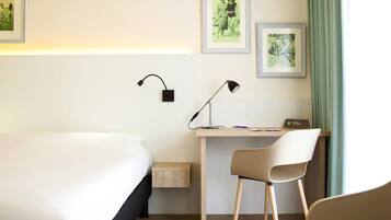 Habitación de hotel con cama, escritorio, silla, dos lámparas de pared y cuadros enmarcados.