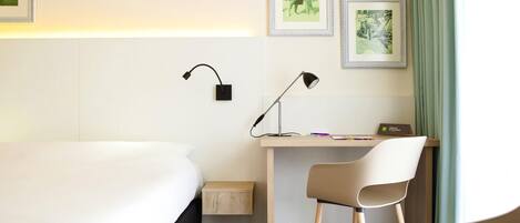 A hotel room with a bed, desk, chair, two wall-mounted lamps, and framed pictures.