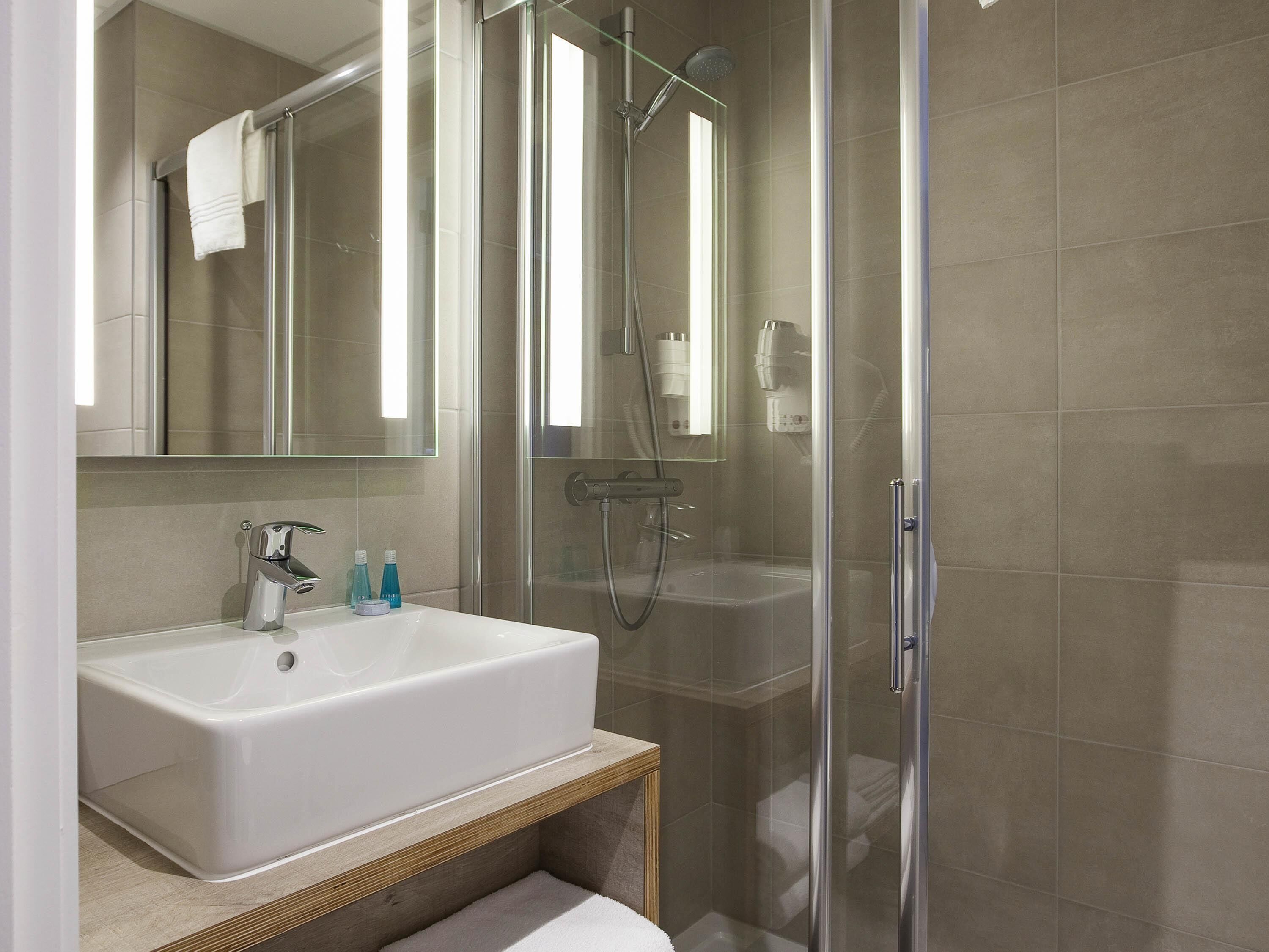 A modern bathroom with a white sink, mirror, and glass-enclosed shower.