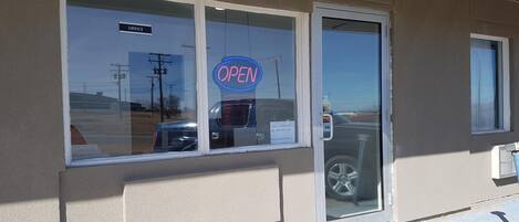 A building with a glass door and windows, a neon 'OPEN' sign, and a 'BUSINESS HOURS' sign.