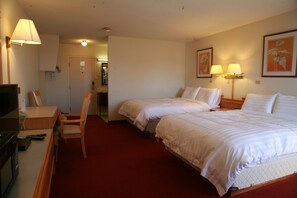 A hotel room with two beds, a desk, a chair, a television, and a red carpet.