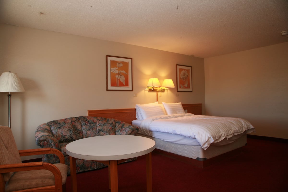 A hotel room with a bed, a round table, a floral sofa, and two wall-mounted lamps.
