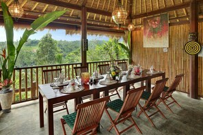 A dining area with a wooden table set for four, surrounded by wooden chairs with green cushions. - Hillside Eden Bali (Payangan)
