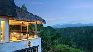 A thatched-roof structure with a balcony overlooking a lush forest and distant mountains. - Hillside Eden Bali (Payangan)