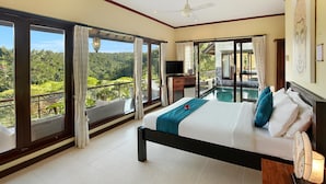 A bedroom with a large bed, a TV, and a view of a lush landscape through large windows. - Hillside Eden Bali (Payangan)