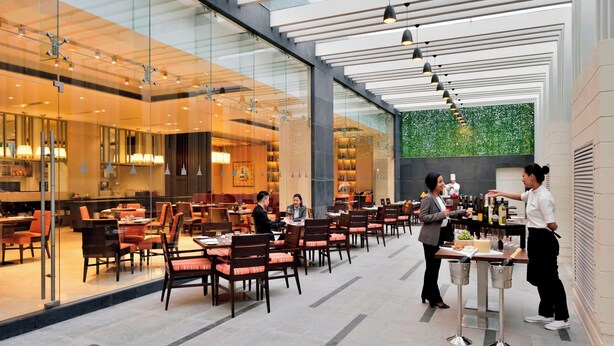 A modern restaurant with glass walls, multiple dining areas, and a green wall decoration.