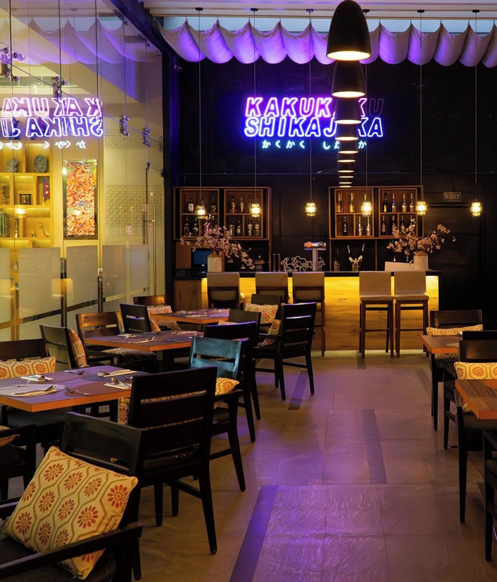 En restaurantindretning med borde, stole, en neonskilte og et barområde.