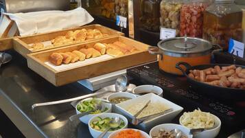Buffet com diversos alimentos, incluindo vegetais, sopa e pães.