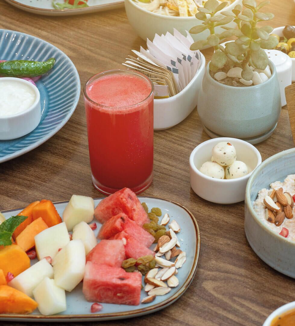 Una mesa con diferentes alimentos, incluyendo un plato de fruta, un vaso de bebida roja y varios cuencos pequeños con distintas preparaciones.
