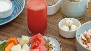 Una mesa con diferentes alimentos, incluyendo un plato de fruta, un vaso de bebida roja y varios cuencos pequeños con distintas preparaciones.