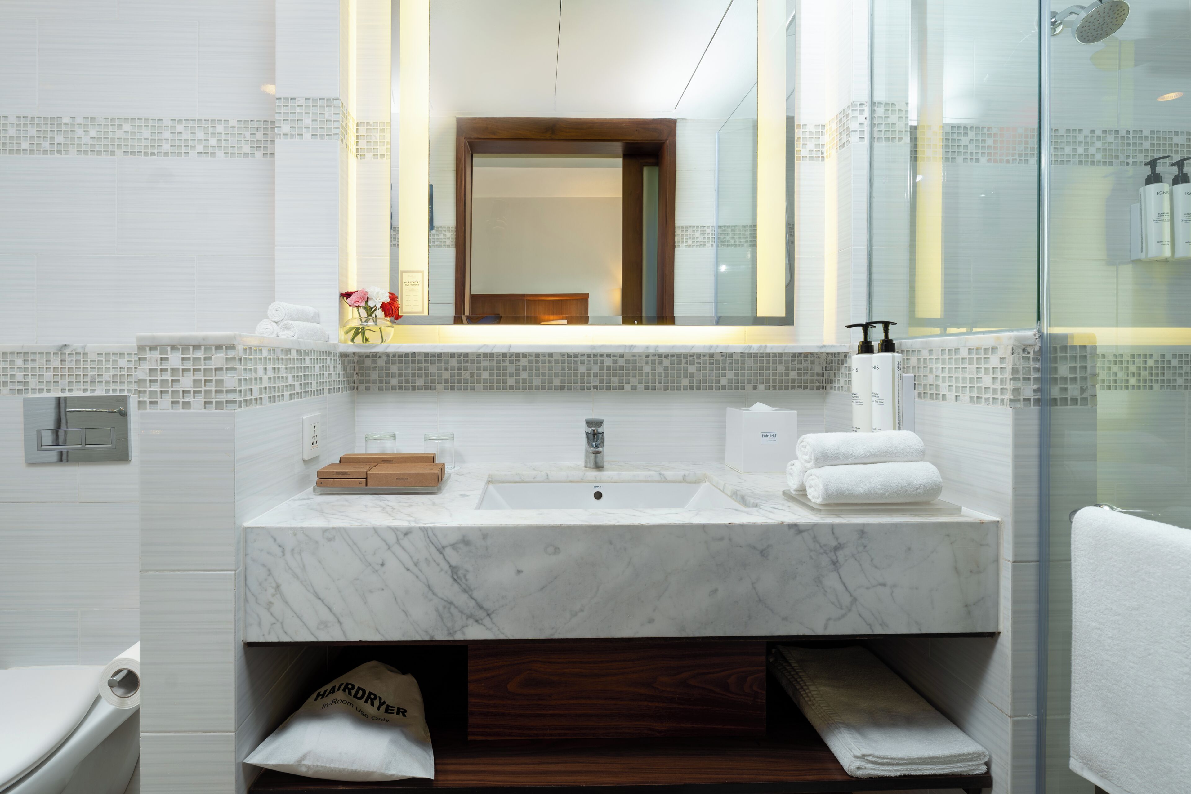 A modern bathroom with a marble sink, a glass shower enclosure, and a wooden vanity.