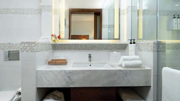 Un baño moderno con lavamanos de mármol, cabina de ducha con paredes de vidrio y tocador de madera.