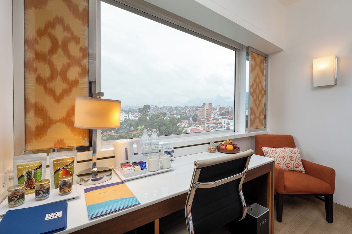 Habitación de hotel con escritorio, silla y vista a la ciudad.