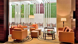 A modern hotel lobby with orange sofas, round tables, and a glass coffee table.