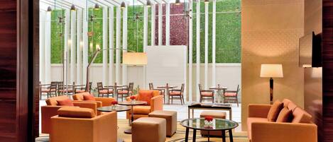 Un moderno vestíbulo de hotel con sofás naranjas, mesas redondas y una mesa de centro de cristal.