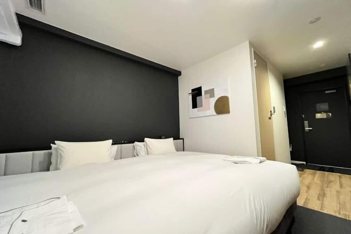 A modern hotel room with a large bed, a dark accent wall, and a minimalist decor.
