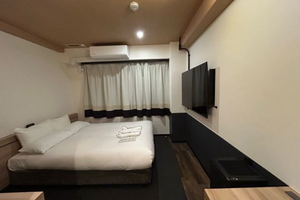 A hotel room with a bed, a flat-screen TV mounted on the wall, and a window with curtains.