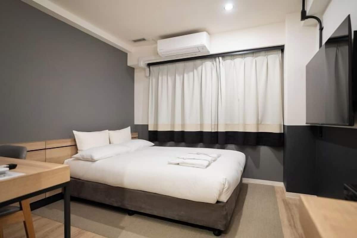 A hotel room with a bed, a desk, an air conditioning unit, and a television.