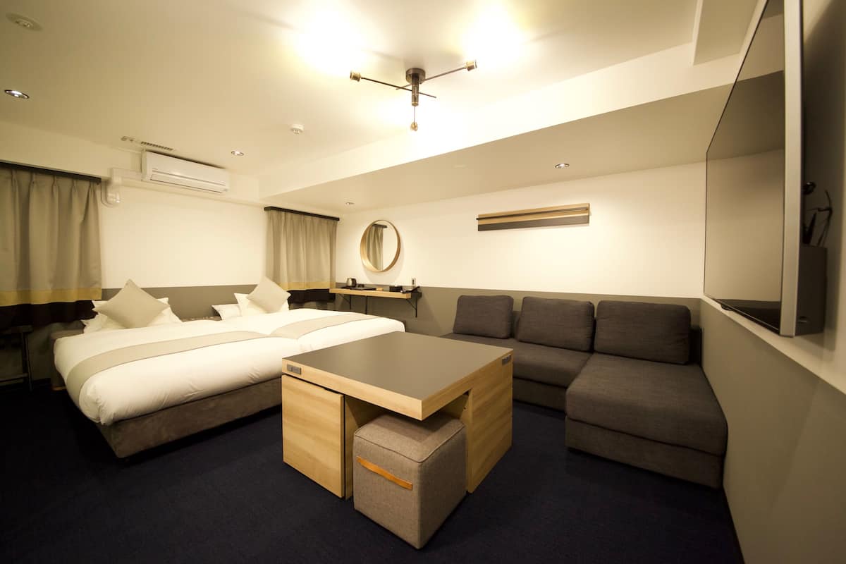 A modern hotel room with a bed, a sofa, a small table, and a TV.