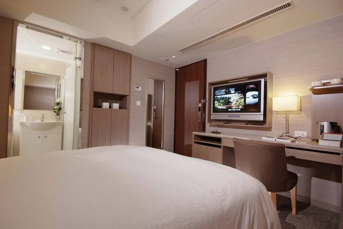 A hotel room with a large bed, a desk with a computer, a television, and a bathroom with a mirror and sink.