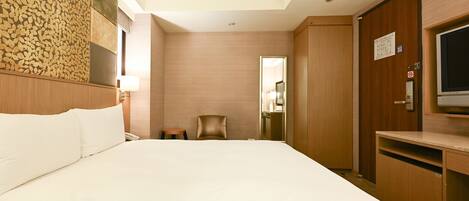 A hotel room with a large bed, a desk with a TV, a chair, and a mirror.