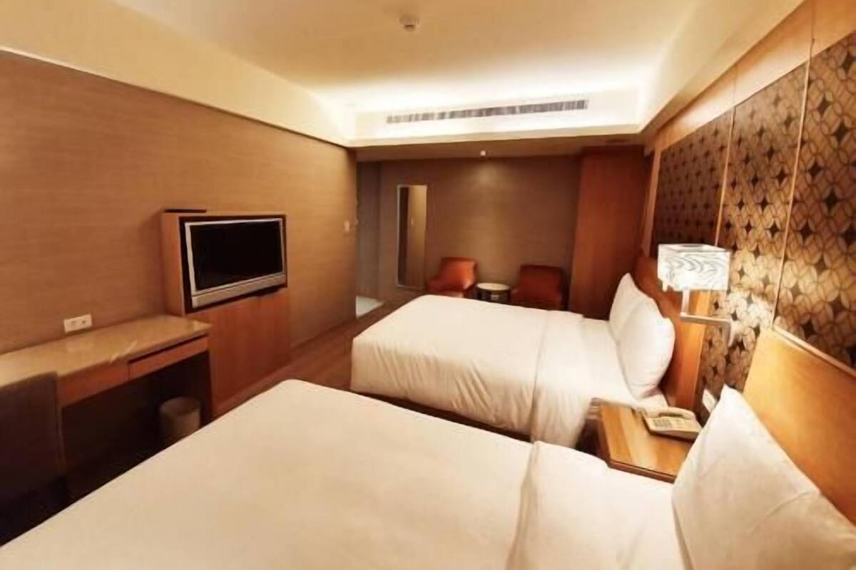 A hotel room with two beds, a desk, a TV, and a lamp.