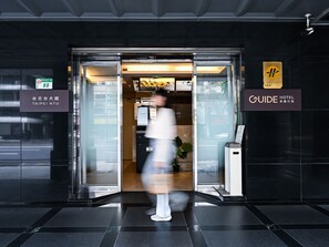 Entrada de un hotel con puerta de cristal, un cartel que dice 'TAIPEI NTU' y un letrero que indica 'GUIDE HOTEL'.