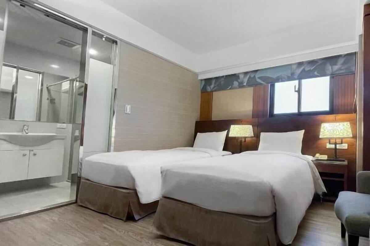 A hotel room with two beds, a bathroom with a sink, and a chair.