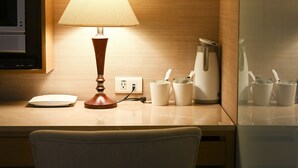 Ein Hotelzimmer mit Schreibtisch, Lampe, Kaffeemaschine und Fernseher.