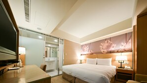 Ein Hotelzimmer mit Bett, Nachttisch, Lampe, Sessel und Fernseher.