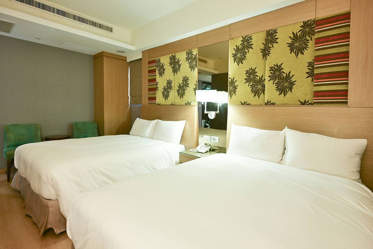 A hotel room with two beds, a mirror, a telephone, and a green chair.