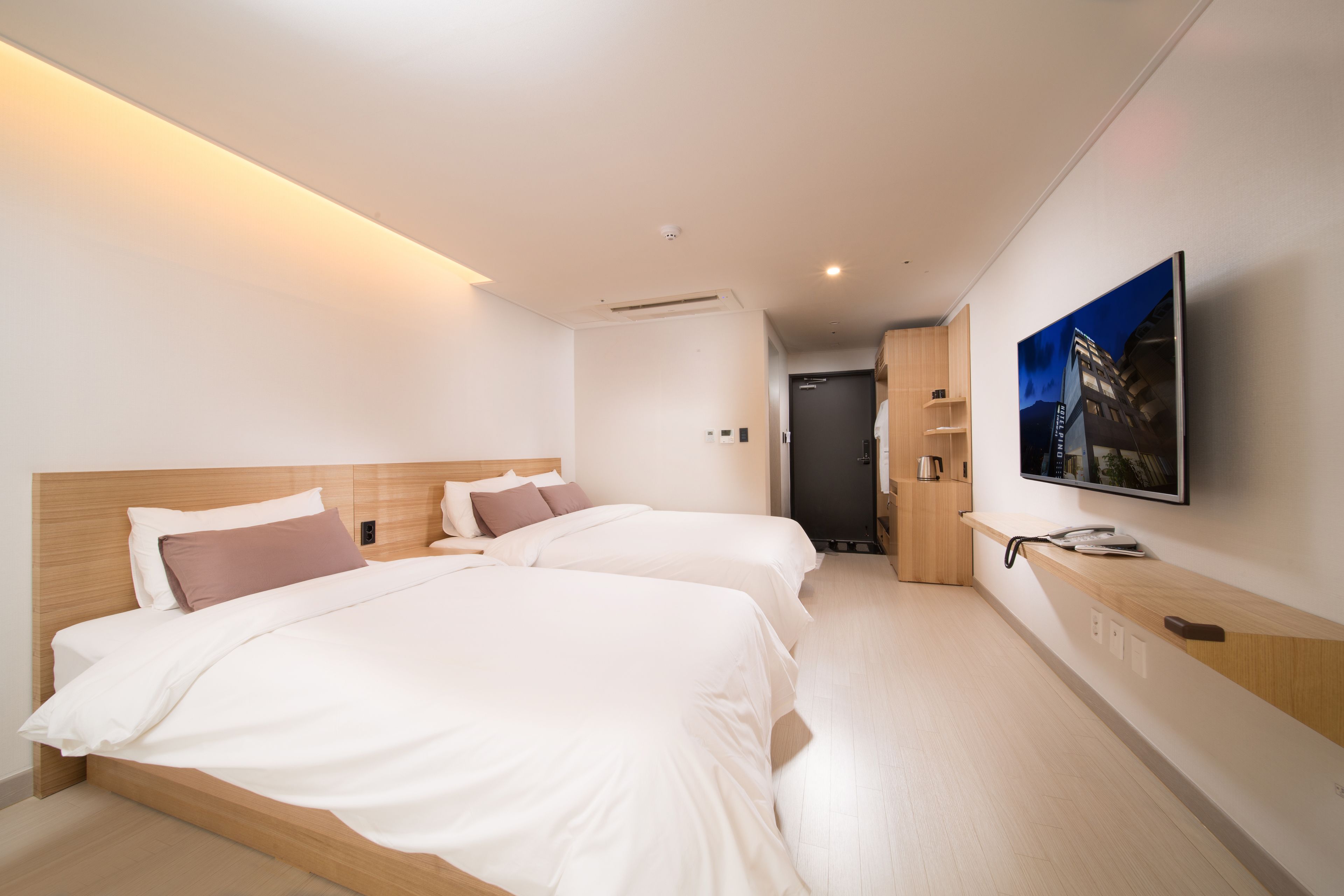 A modern hotel room with two beds, a flat-screen TV, a wooden headboard, and a small kitchenette.