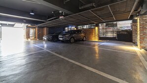 A parking garage with two cars parked, concrete floors, and a brick wall. - Busan station Popcorn Hotel (Busan)