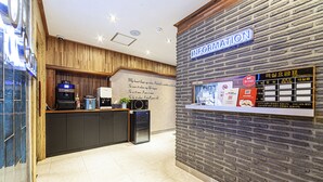 A reception area with a wooden counter, a coffee machine, a refrigerator, and a wall with an information sign. - Busan station Popcorn Hotel (Busan)