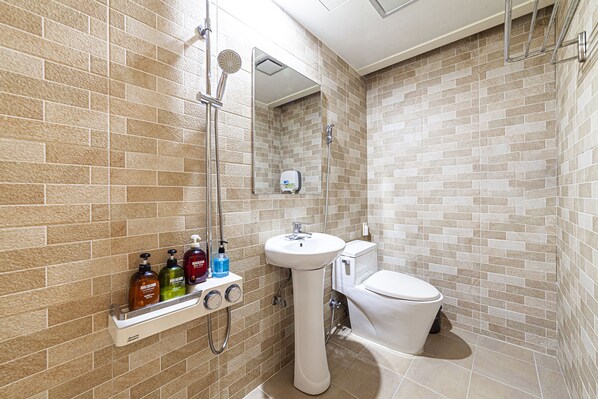 Un baño con pared de azulejos color beige, un lavamanos blanco pedestal, un inodoro y una ducha con cabezal de ducha manual.