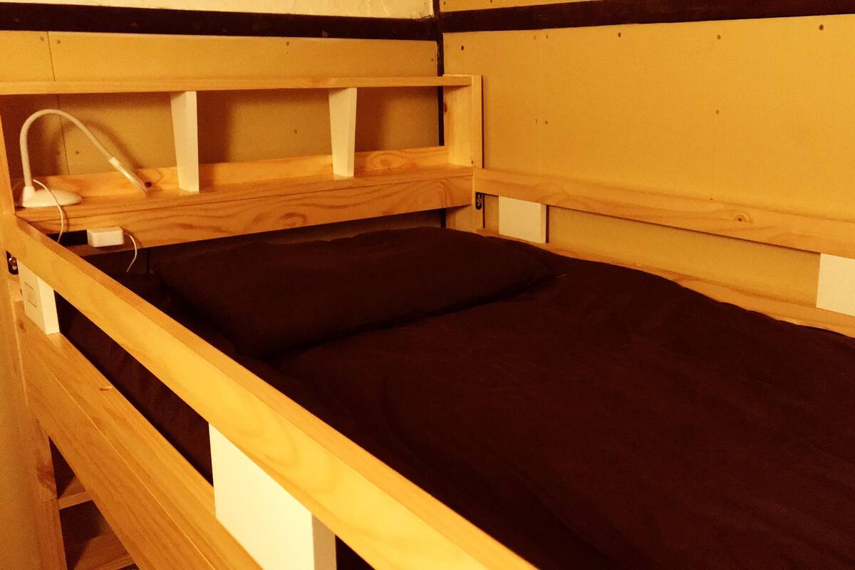 A wooden bunk bed with a headboard, a bedside table, and a lamp.