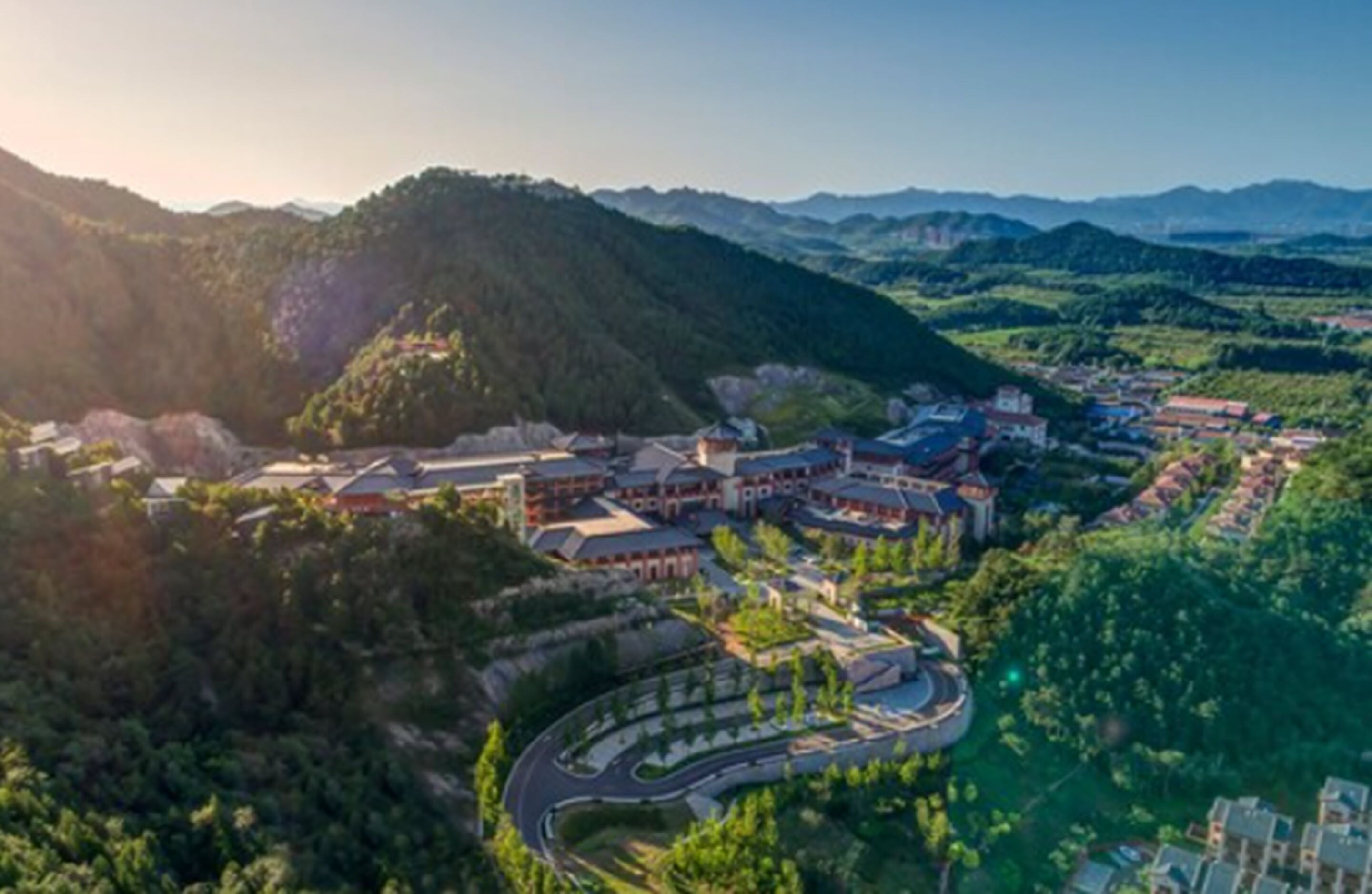 An aerial view of a resort with multiple buildings, a winding road, and lush greenery.